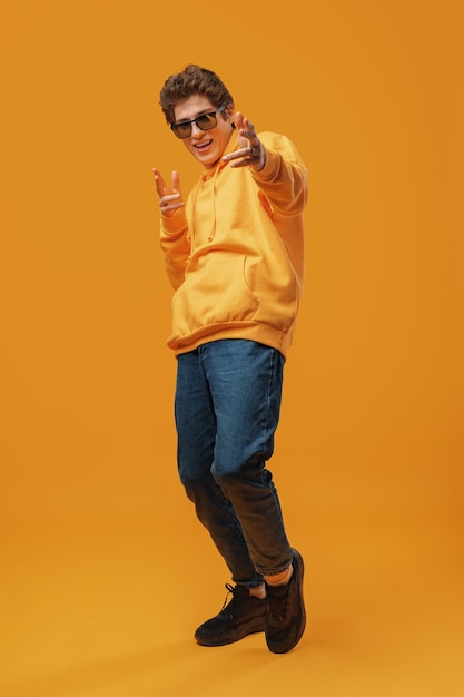 Handsome young man poses in sweatshirt and sunglasses on a yellow background
