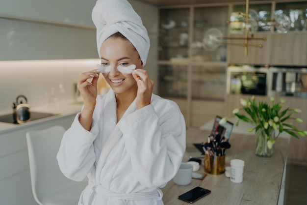 Photo happy woman in bathrobe removes collagen patches smiles during athome beauty routine personal care joy