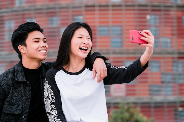 Happy young asian couple taking selfie with smartphone on city street