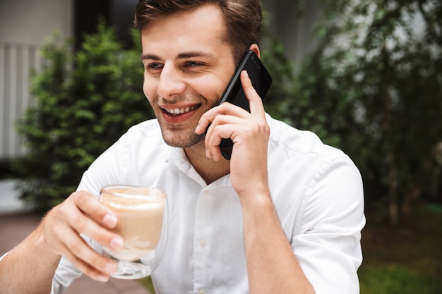 Happy young businessman dressed in shirt drinking coffee