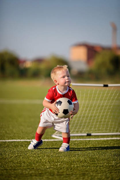 Счастливый малыш мальчик играет в футбол с мячом на поле возле ворот