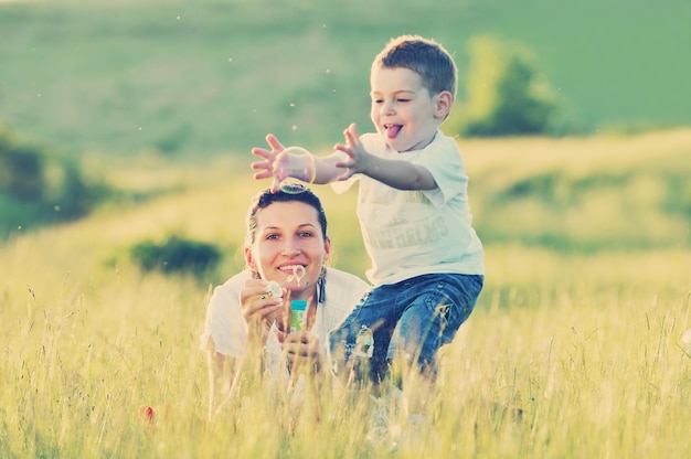 Счастливый ребенок и женщина на открытом воздухе играют с мыльным пузырем на лугу
