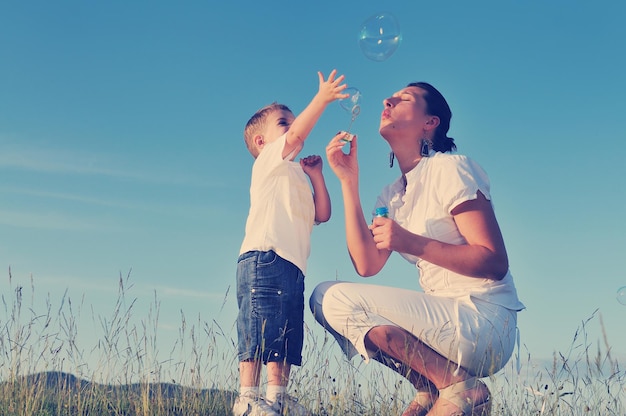 Счастливый ребенок и женщина на открытом воздухе играют с мыльным пузырем на лугу