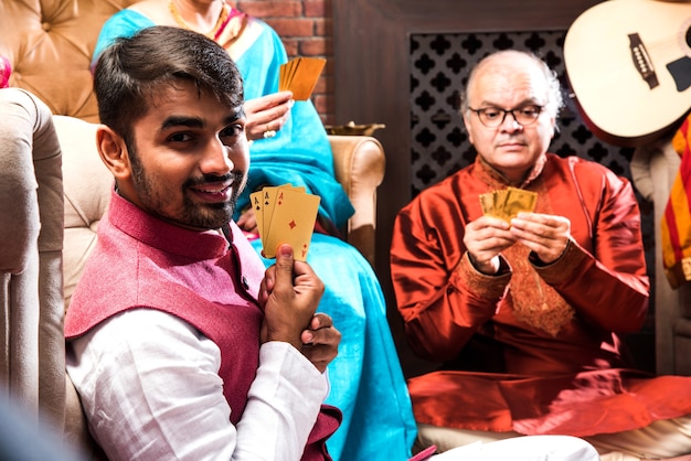 Счастливая индийская семья играет в подростковую игру «Патти или три карты» в ночь фестиваля дивали в традиционной одежде дома