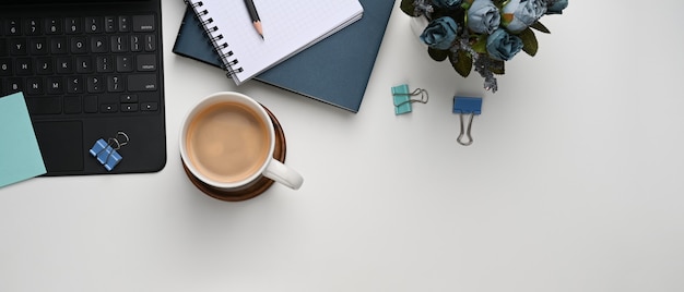 Фото Горизонтальное изображение белого офисного стола с кофейной чашкой, заводом, ноутбуком и клавиатурой.