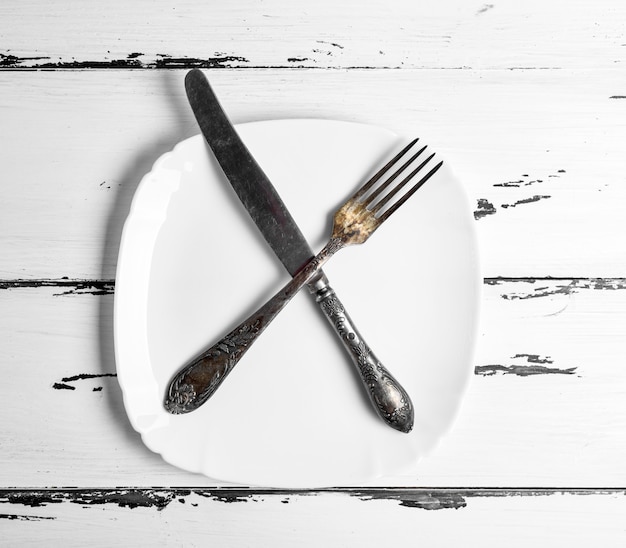 写真 空白の白い正方形のプレートの上に横たわるナイフで鉄のビンテージフォーク