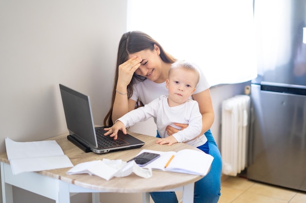 Jonge vrouw die thuis werkt met een laptop met een baby op zijn handen