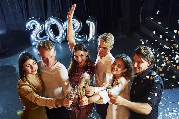 Стукнутые очки. Веселая группа людей с напитками в руках празднует новый 2021 год.