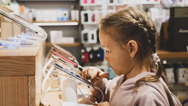 Маленький ребенок с помощью нового смартфона на прилавке в магазине электроники.