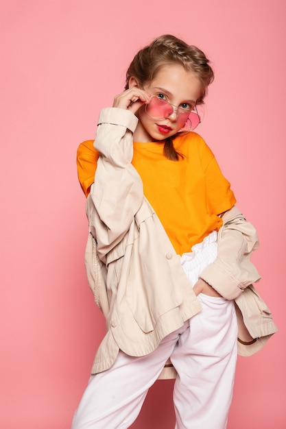Little girl in pink glasses. Trendy fashion style stylish funtime concept. Vertical full-size full-length portrait of laughing cute sweet adorable lovely charming girl isolated pink wall