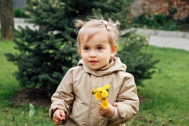Фото Маленькая малышка в плаще собирает желтые одуванчики в весеннем саду милая девочка