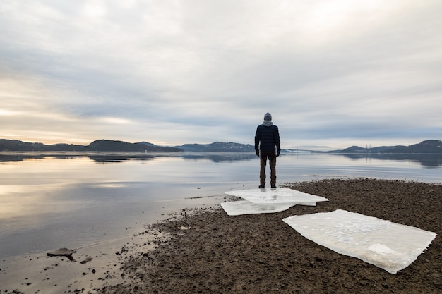 Фото Человек, стоящий на пляже, льдины на темном песке, спокойное море, туман и туман. хамресанден, кристиансанн, норвегия