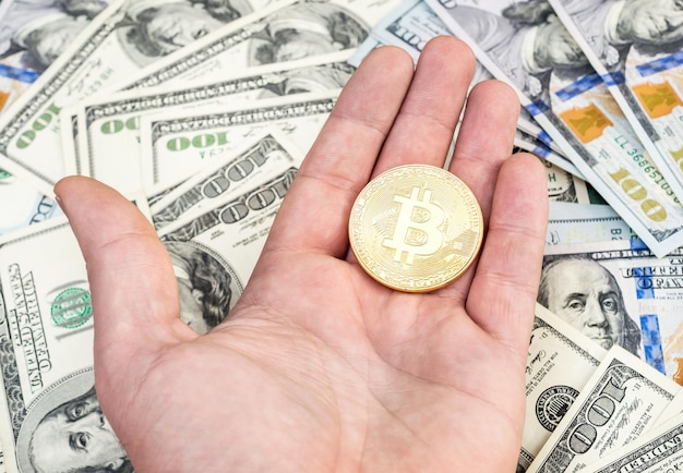 Man's hand met gouden bitcoin over de achtergrond van Amerikaanse dollars
