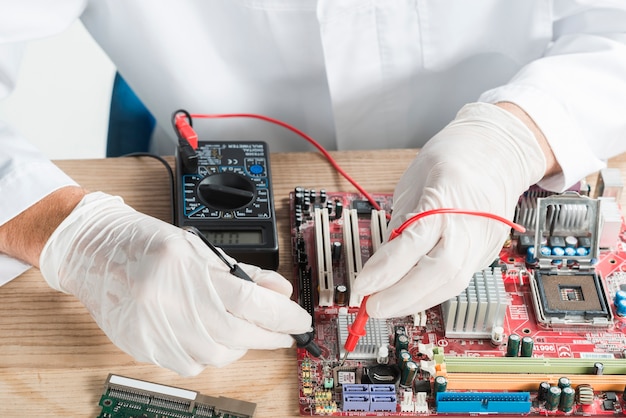 Male technician examining computer motherboard with digital multimeter