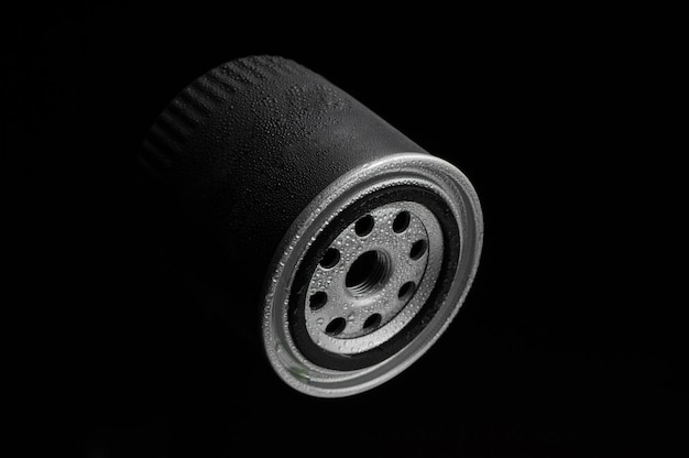 Metallic automotive filter cylindrical shape with drops of water on a black background close up