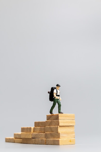 Фото Миниатюрный путешественник людей, стоящий на деревянном блоке на сером фоне. концепция путешествий и приключений