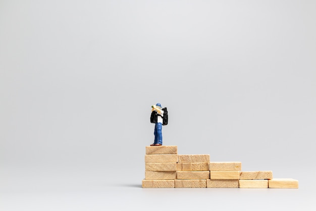 Фото Миниатюрный путешественник людей, стоящий на деревянном блоке на сером фоне. концепция путешествий и приключений
