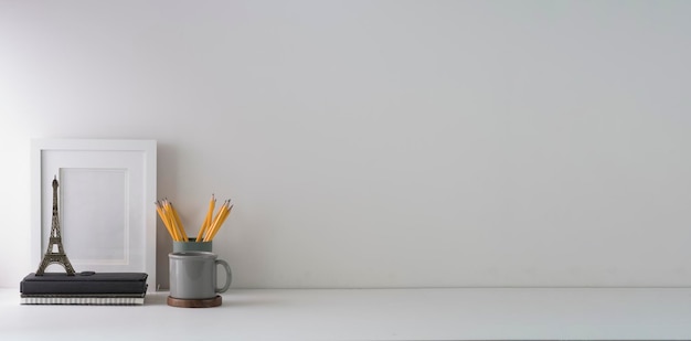 Фото Минимальное рабочее место с пустой рамкой для книги, кофейной чашкой и держателем для карандашей на белом столе скопируйте место для текста