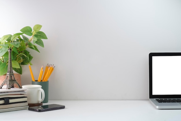 Фото Минимальное рабочее место с ноутбуком, кофейной чашкой, комнатным растением и канцелярскими принадлежностями на белом столе скопируйте место для текста