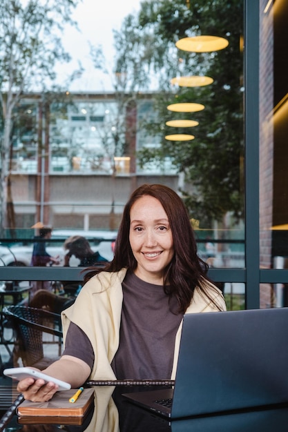 Photo middle aged woman with laptop and smartphone in cafe outdoor smiling at camera vertical