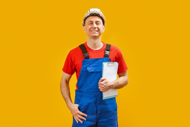 Фото Инженер средних лет в белом шлеме кладет руку в карман, улыбается и смотрит в камеру, изолированную на желтом фоне.