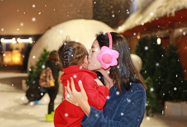 Мать целует дочь в снегу, зимнее время.