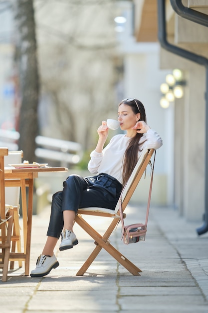 사진 화창한 날에 카페 테라스에 앉아서 커피를 마시는 잠겨있는 젊은 여자.