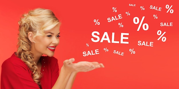Фото Люди, праздники, распродажа, покупки и рекламная концепция - милая женщина в красной одежде держит что-то на ладонях на красном фоне с распродажей и процентными знаками