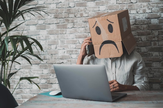 Photo people at work with sad carton box on head diong phone call in front of a laptop on the desk sad worker anonymous business fail activity and unhappy leisure activity online idendity lost