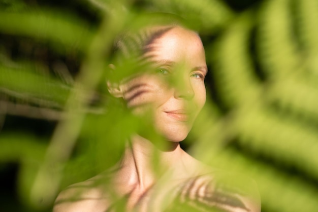 Foto ritratto di una donna con la testa rasata con le ombre di una felce nella ripresa naturale della foresta