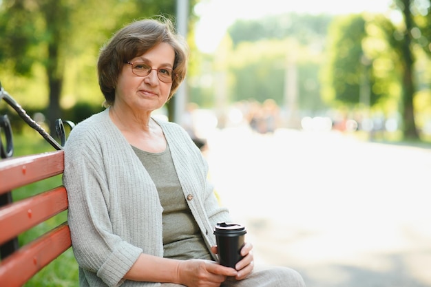 Photo portrait of aged positive peaceful lady sitting bench hold coffee