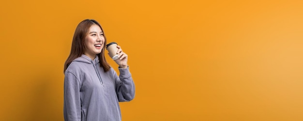 Портрет красивой азиатской женщины, держащей бумажную кофейную чашку на изолированном желтом фоне портретная концепция, используемая для рекламы и вывесок, изолированных на синем фоне копировального пространства