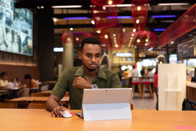Портрет красивого молодого темнокожего мужчины с ноутбуком в кафе