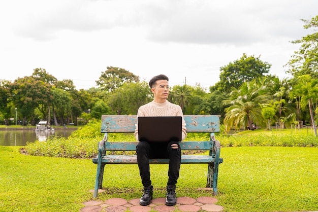 Портрет красивого молодого человека в парке летом с помощью портативного компьютера