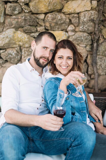 Photo portrait of happy couple with wineglasses sitting against stone wall