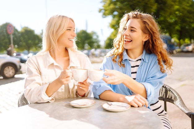 Портрет улыбающейся молодой женщины с друзьями, сидящей на открытом воздухе в кафе, пьющей кофе.