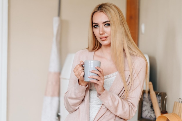 Portret van een blank meisje met make-up zit in de keuken Goedemorgen met een kopje aromatische koffie