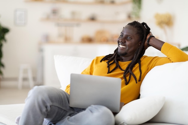 Portret van lachende zwarte man met laptop ontspannen in de stoel thuis