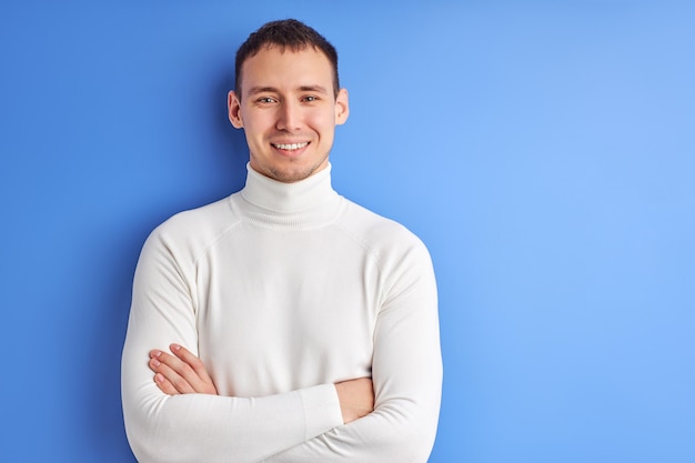 Foto portret van man in casual wit overhemd poseren met armen gevouwen, glimlachen en kijken naar camera geïsoleerd op blauwe achtergrond.