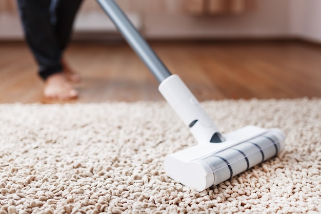 Photo powerful cordless vacuum cleaner with white cyclonic dust collection technology in hand, cleans the carpet in the house near the sofa. close-up