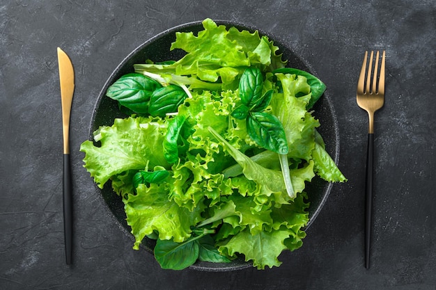 Photo a plate with fresh lettuce and basil leaves on a dark background