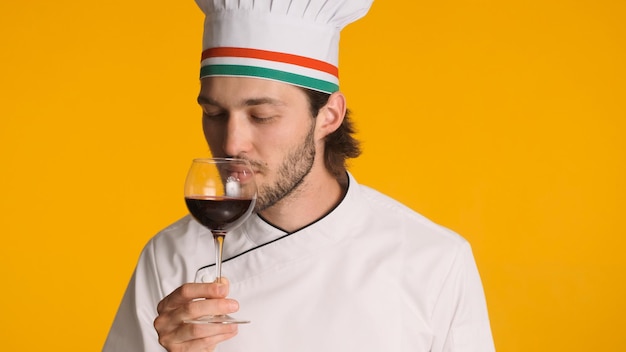 Professionele chef-kok gekleed in uniform met glas wijn geïsoleerd op gele achtergrond Man sommelier snuiven van wijn