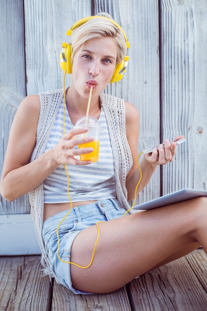 Pretty blonde woman listening music with her mobile phone and drinking orange juice