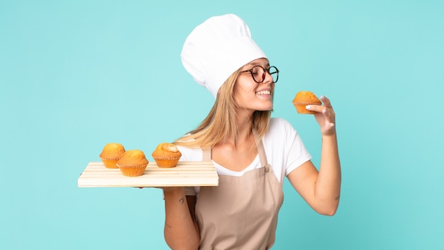 Фото Довольно молодая блондинка шеф-повар женщина держит поднос кексов
