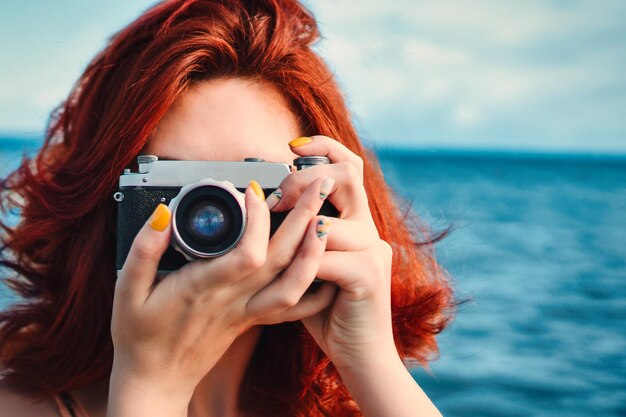 Фото Красноволосая женщина, путешествующая фотографом, фотографирует на фоне моря.