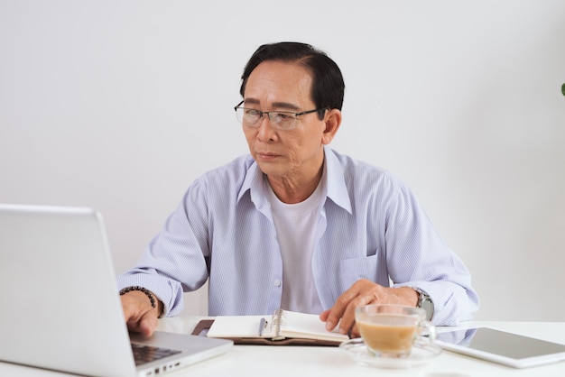 Senior man aan het werk met laptop en basisdingen voor werk aan zijn bureau