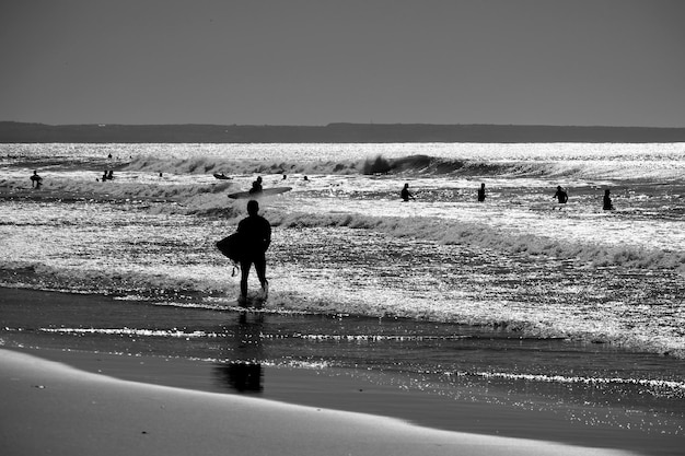 写真 海岸でサーフボードで歩いているシルエットの男性