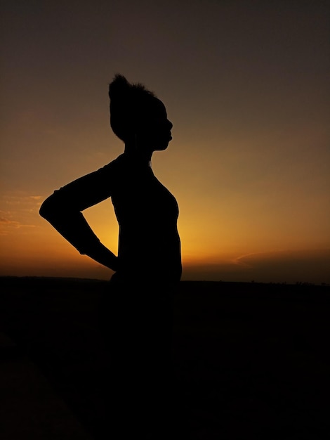 Фото Силуэт женщины, стоящей на берегу напротив неба во время захода солнца