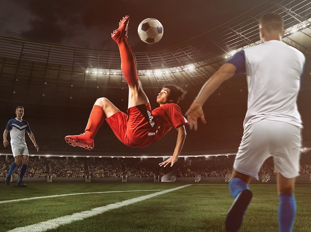 Фото Нападающий футбола в красной форме бьет по мячу акробатическим ударом в воздухе на стадионе