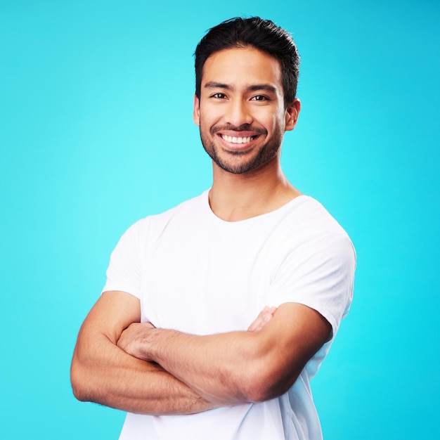 Photo smile happy and portrait of asian man arms crossed with casual fashion isolated in a studio blue background relax calm and young male person proud or confident mindset natural and happiness